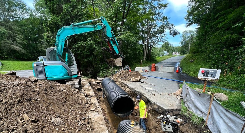 Excavator laying large drain pipe along a road